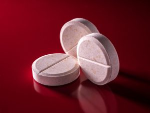 Drei runde, weisse Tabletten mit Bruchkerbe liegen nebeneinander auf rotem Hintergrund. Dosierung und Einnahmezeit von ADHS-Medikamenten legt die behandelnde Ärztin oder der Arzt fest.