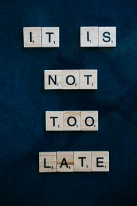 Scrabble-Steine bilden die Worte „It is not too late“ auf dunklem Hintergrund.
