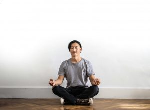Ein Mann sitzt im Schneidersitz, die Augen geschlossen, in tiefer Konzentration. Die klare, minimalistische Umgebung fördert die innere Ruhe.