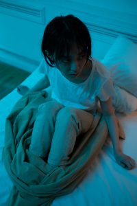 Eine Person sitzt angespannt in einem dunklen Schlafzimmer, die Augen weit geöffnet, möglicherweise geplagt von innerer Unruhe oder Schlafproblemen.