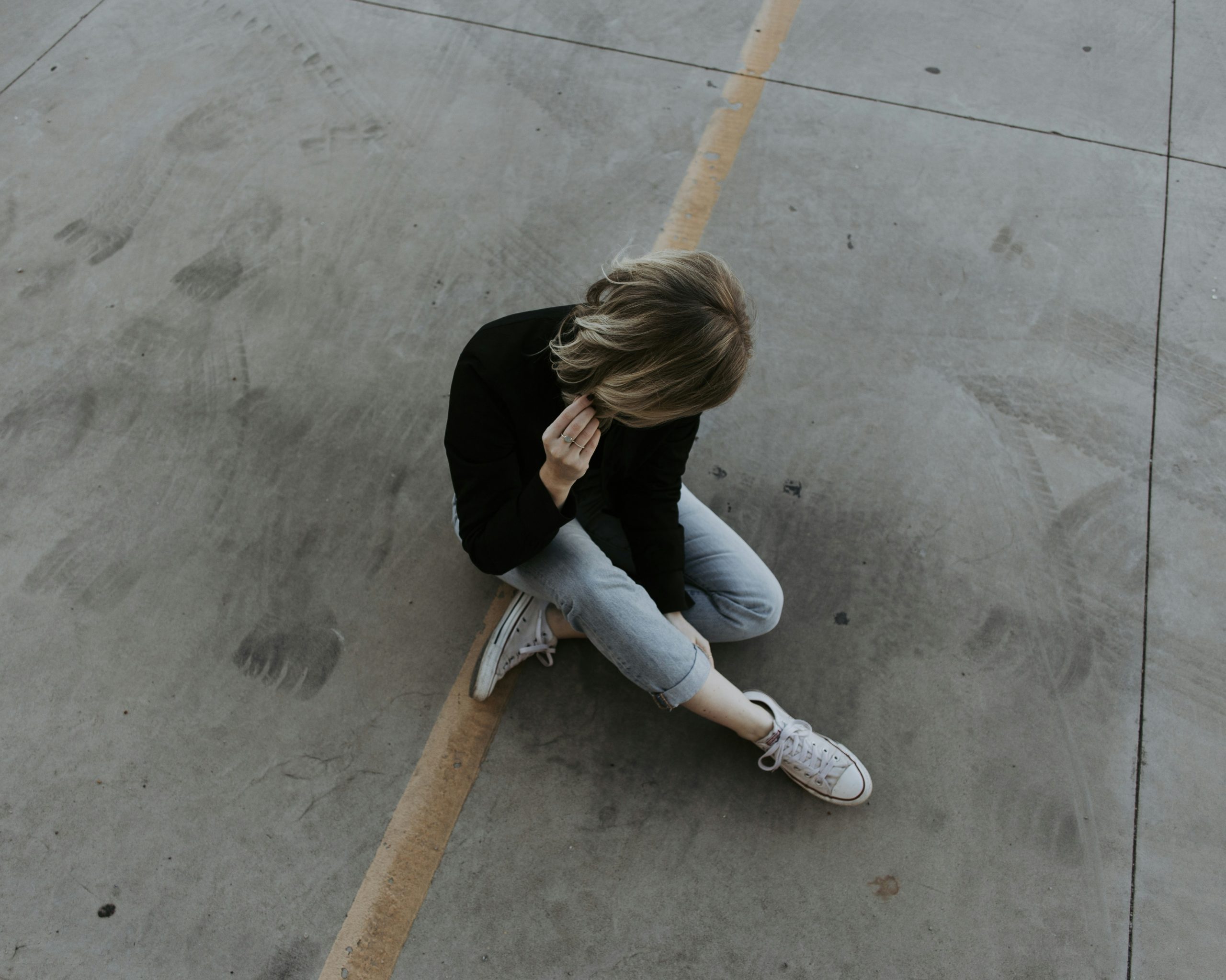 Eine junge Person sitzt allein auf dem Boden und hält sich nachdenklich den Kopf – ein Ausdruck von innerer Anspannung oder Erschöpfung. Dieses Bild symbolisiert die emotionale Überforderung, die viele Menschen mit ADHS in der Schweiz erleben, besonders in stressigen Alltagssituationen.