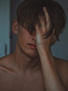 Ein junger Mann verdeckt sein Gesicht mit der Hand. Müdigkeit, Frustration oder innere Unruhe spiegeln sich in seiner Haltung.
