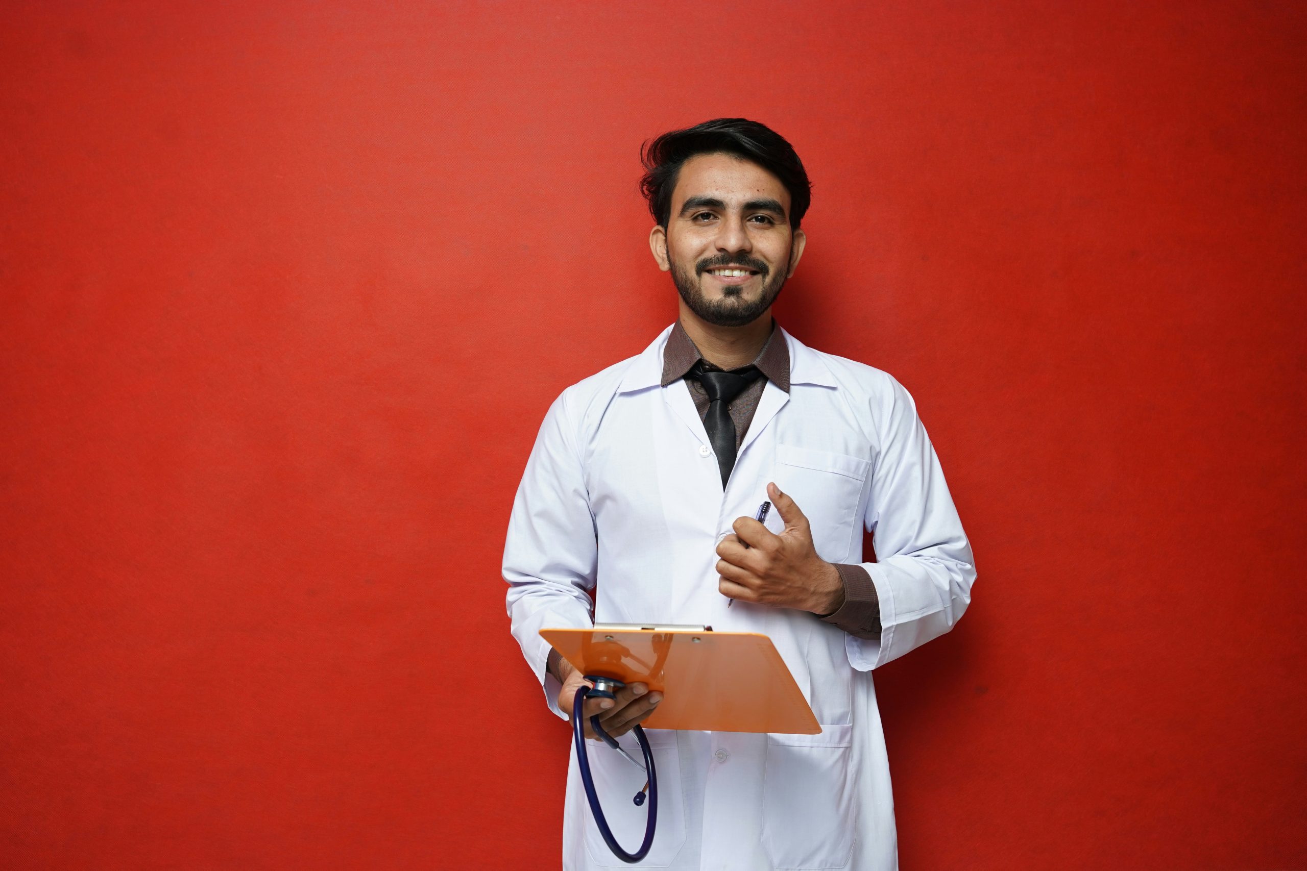 Ein Arzt in weissem Kittel steht vor einer roten Wand und hält eine Patientenmappe in der Hand. Das Bild symbolisiert die ärztliche Qualitätssicherung auf klaro-adhs.ch und den Fokus auf medizinisch geprüfte ADHS-Behandlung in der Schweiz.