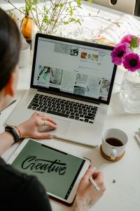 Ein Arbeitsplatz mit digitalen Geräten, kreativen Projekten und einem Blumenarrangement. Ein gestalteter Arbeitsplatz kann helfen, im Beruf fokussiert zu arbeiten.