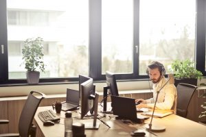 Ein konzentrierter Mitarbeiter arbeitet im modernen Büro mit mehreren Monitoren und Headset. Strukturierte Arbeitsumgebungen und Hilfsmittel können Menschen mit ADHS helfen, im Beruf fokussiert zu bleiben.