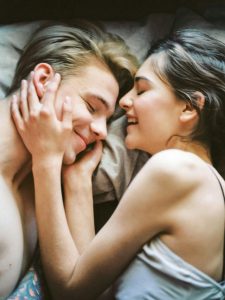 Ein junges Paar liegt entspannt im Bett und zeigt Zuneigung und Nähe. Solche Momente der Verbundenheit sind wichtig, wenn ADHS die Beziehung belastet.