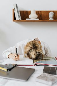 Eine junge Frau hat den Kopf auf ein offenes Buch gelegt und wirkt erschöpft