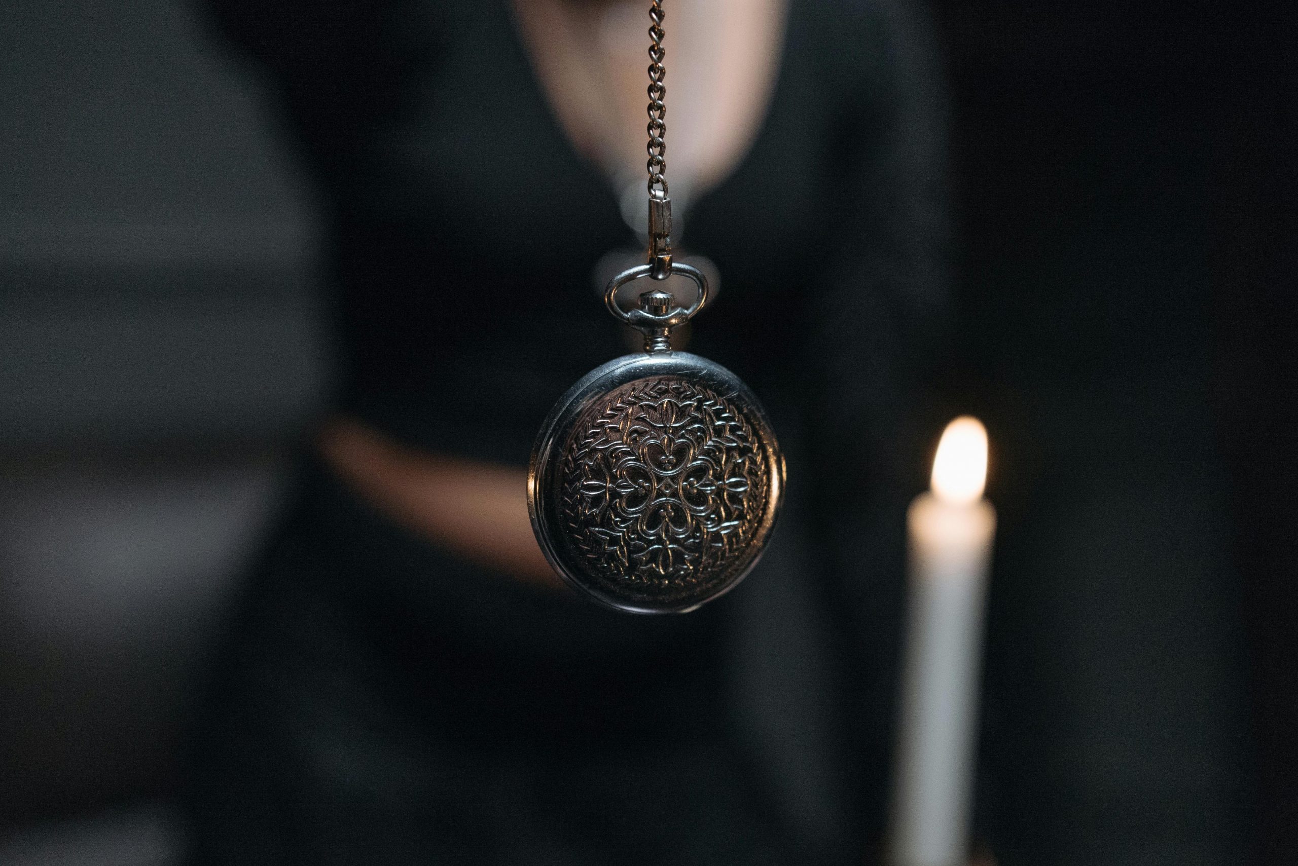 Eine antike Taschenuhr pendelt vor einer brennenden Kerze – ein klassisches Symbol der Hypnose. Dieses Bild steht exemplarisch für Methoden der ADHS Hypnose Schweiz, die auf visuelle Fokussierung setzen.
