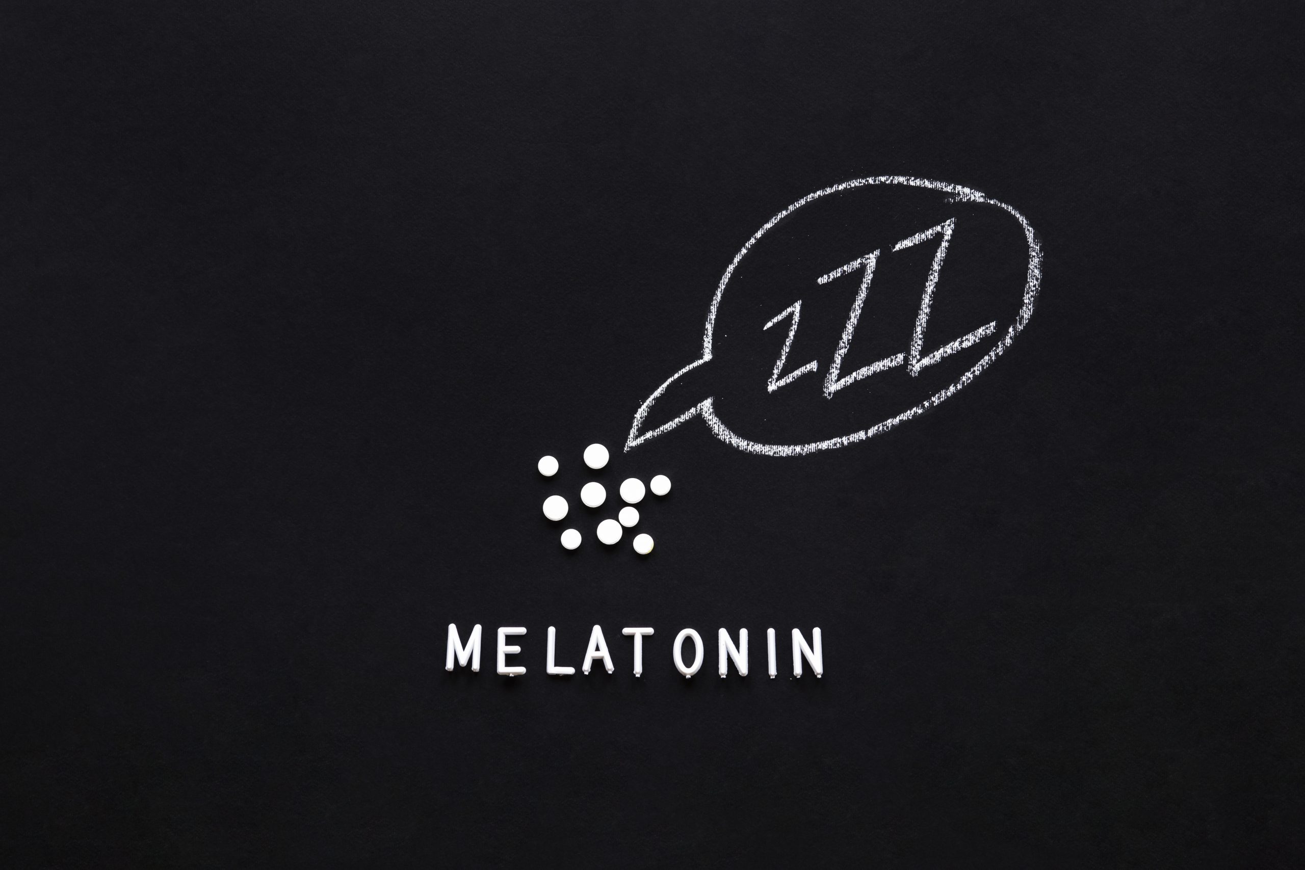 Auf schwarzem Hintergrund sind weisse Tabletten und das Wort „Melatonin“ angeordnet, daneben eine Sprechblase mit „ZZZ“, gezeichnet in Kreide. Das Bild symbolisiert den Einsatz von Melatonin zur Unterstützung des Schlafs. Bei ADHS Schweiz wird Melatonin oft als natürliche Einschlafhilfe diskutiert.