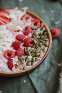 Eine bunte Smoothie Bowl mit frischen Himbeeren, knackigen Kürbiskernen und Kokoschips, liebevoll angerichtet. Eine nährstoffreiche Mahlzeit kann eine ausgewogene Ernährung unterstützen.
