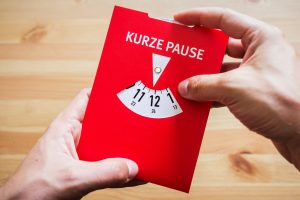 Zwei Hände halten eine rote Parkscheibe, auf der „Kurze Pause“ steht, und stellen die Zeit ein. Regelmässige Erholungsphasen unterstützen Aufmerksamkeit und Leistungsfähigkeit im Alltag.