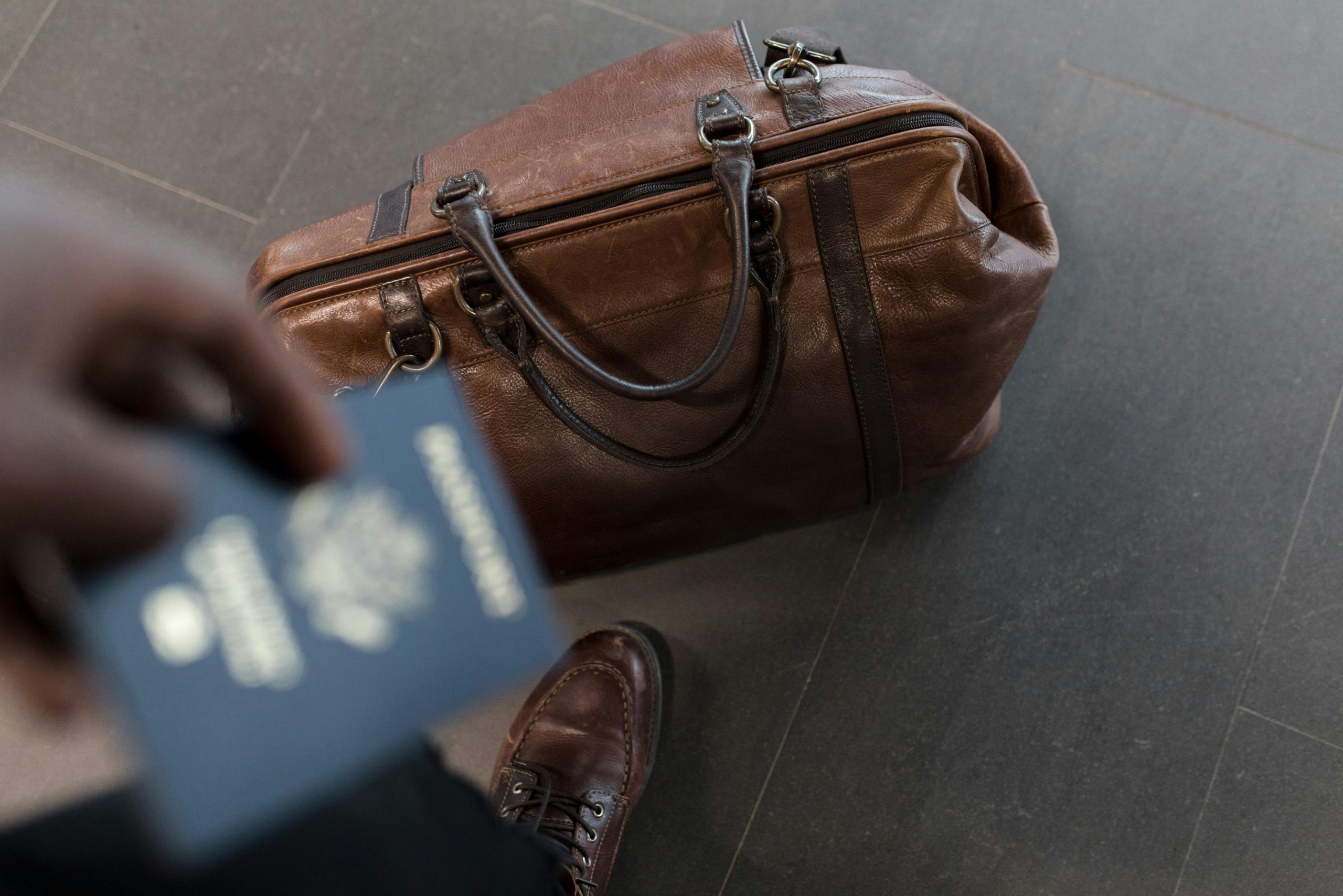 Ein Pass und eine braune Reisetasche am Flughafen deuten auf eine bevorstehende Reise hin. Besonders bei ADHS-Betroffenen in der Schweiz kann das Reisen Stress und Reizüberflutung auslösen – gute Vorbereitung ist der Schlüssel zur Entlastung.