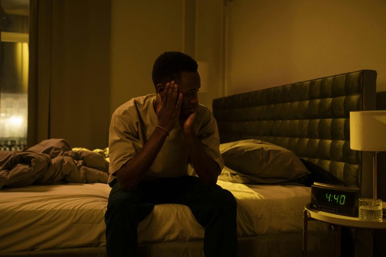 Ein Mann sitzt mitten in der Nacht erschöpft auf seinem Bett und stützt den Kopf in die Hände, während der Wecker 4:40 Uhr anzeigt. Schlaflosigkeit wie diese kann ein häufiges Begleitsymptom bei ADHS in der Schweiz sein. Viele Betroffene berichten von unruhigen Nächten und frühem Erwachen.