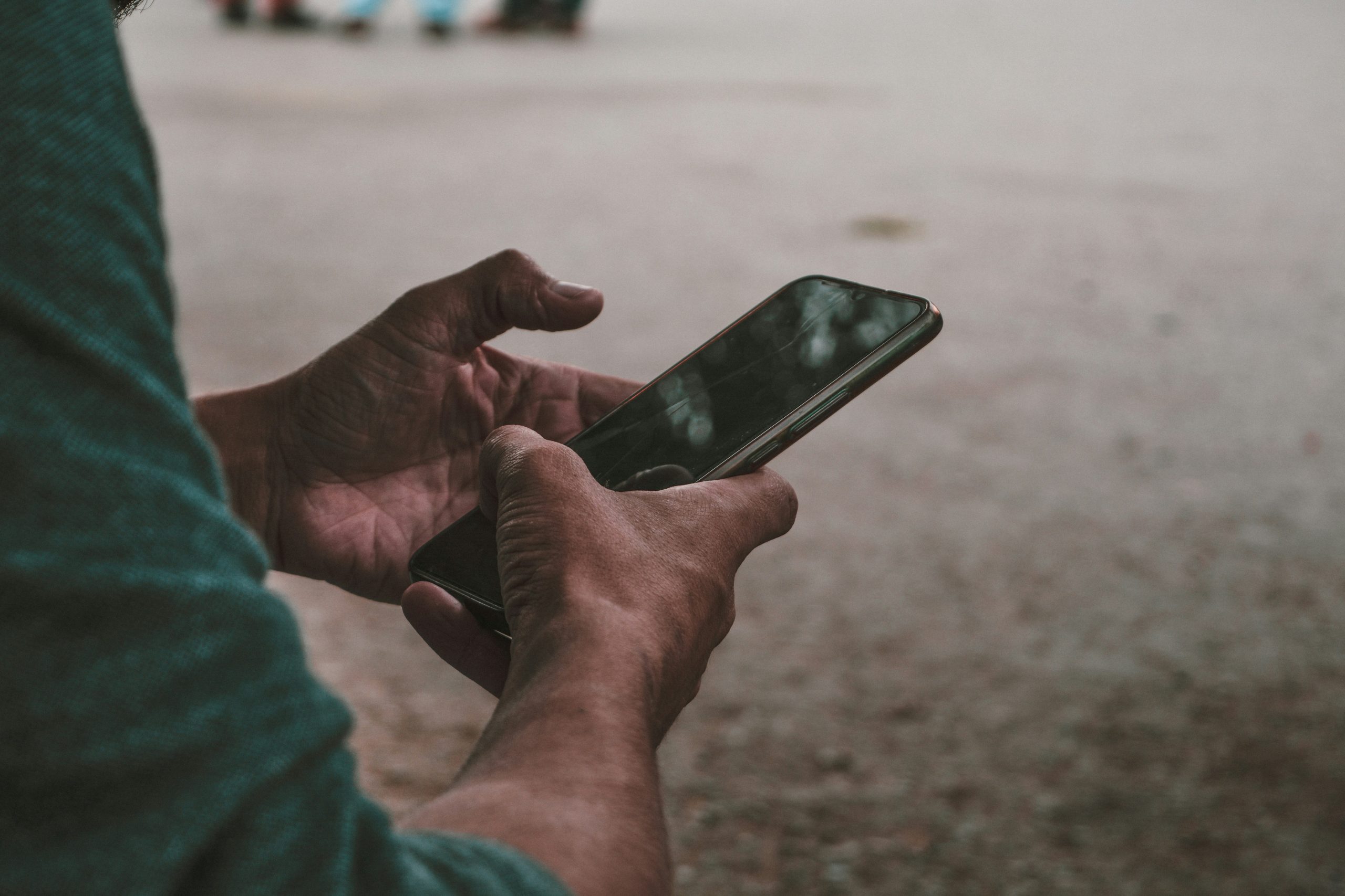Nahaufnahme von zwei Händen, die ein Smartphone halten, während die Person im Freien sitzt. Der Blick ist auf das Display gerichtet, der Fokus auf digitale Inhalte liegt im Vordergrund. Im Zusammenhang mit ADHS Schweiz zeigt dieses Bild, wie auch unterwegs die Nutzung digitaler Geräte zur Reizüberflutung führen kann.