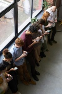 Eine Gruppe junger Menschen steht nebeneinander und blickt konzentriert auf ihre Smartphones.