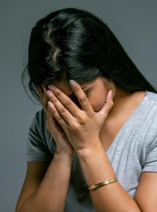 Eine Frau verbirgt ihr Gesicht in den Händen und wirkt überwältigt von ihren Gefühlen. Das Bild steht für emotionale Überforderung.