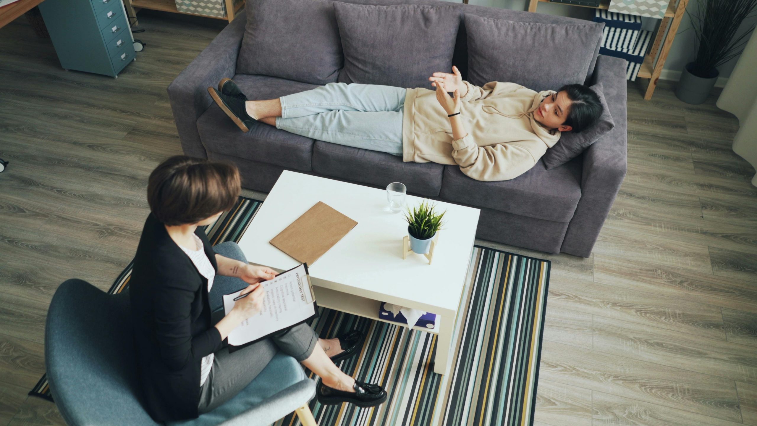 Eine Person liegt auf einem Therapiesofa, während eine Therapeutin aufmerksam Notizen macht – ein klassisches Bild für psychologische Begleitung. Für viele Menschen mit ADHS in der Schweiz ist die Psychotherapie ein wichtiger Schritt, um emotionale Stabilität zu erreichen und individuelle Strategien gegen Reizüberflutung zu entwickeln.
