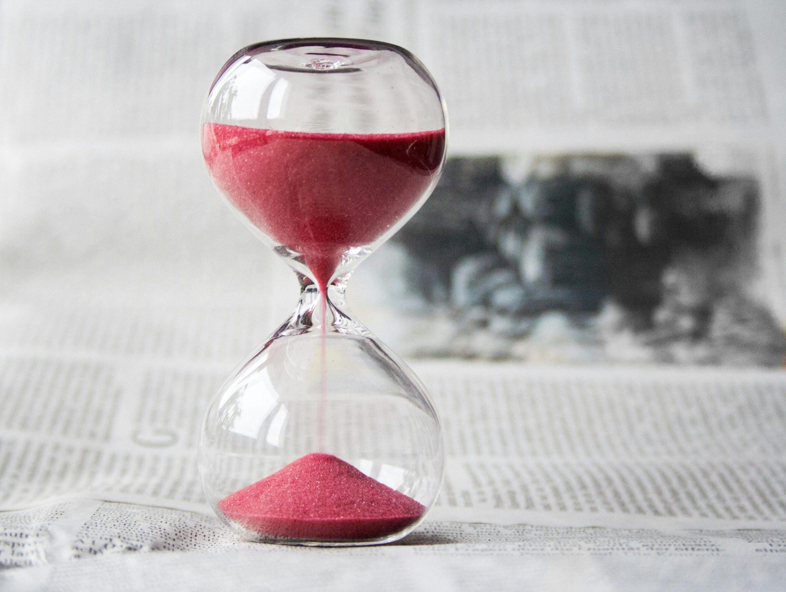 Die rote Sanduhr läuft langsam durch und symbolisiert das Vergehen von Zeit. Gerade bei ADHS im Beruf in der Schweiz ist ein bewusster Umgang mit Zeitressourcen ein zentraler Faktor für einen ausgeglichenen Arbeitsalltag.