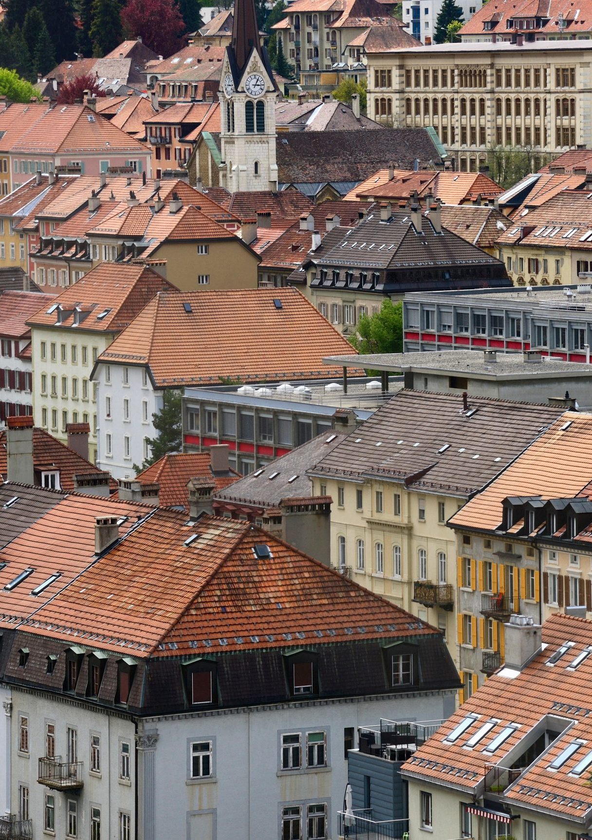 Blick auf das streng geometrisch angelegte Stadtzentrum von La Chaux-de-Fonds, links der Turm des Temple De L'abeille, UNESCO-Weltkulturerbe. La Chaux-de-Fond im Kanton Neuenburg liegt im Juragebirge auf einer Höhe von 1000 m, wenige Kilometer südlich der französischen Grenze. Nach Genf, Lausanne und Freiburg ist es die viertgrösste Stadt im französischsprachigen Teil des Landes. Das Wachstum und der Wohlstand der Stadt sind hauptsächlich mit der Uhrenindustrie verbunden, sie ist das wichtigste Zentrum der Uhrenindustrie in der als Watch Valley bekannten Region. Die Stadt ist nicht nur für ihre Uhrenindustrie bekannt, sondern auch für ihr städtebauliches Konzept der parallel verlaufenden Strassen, das das Bedürfnis der Uhrmacher nach einer rationalen Organisation widerspiegelt, Schweiz, Europa