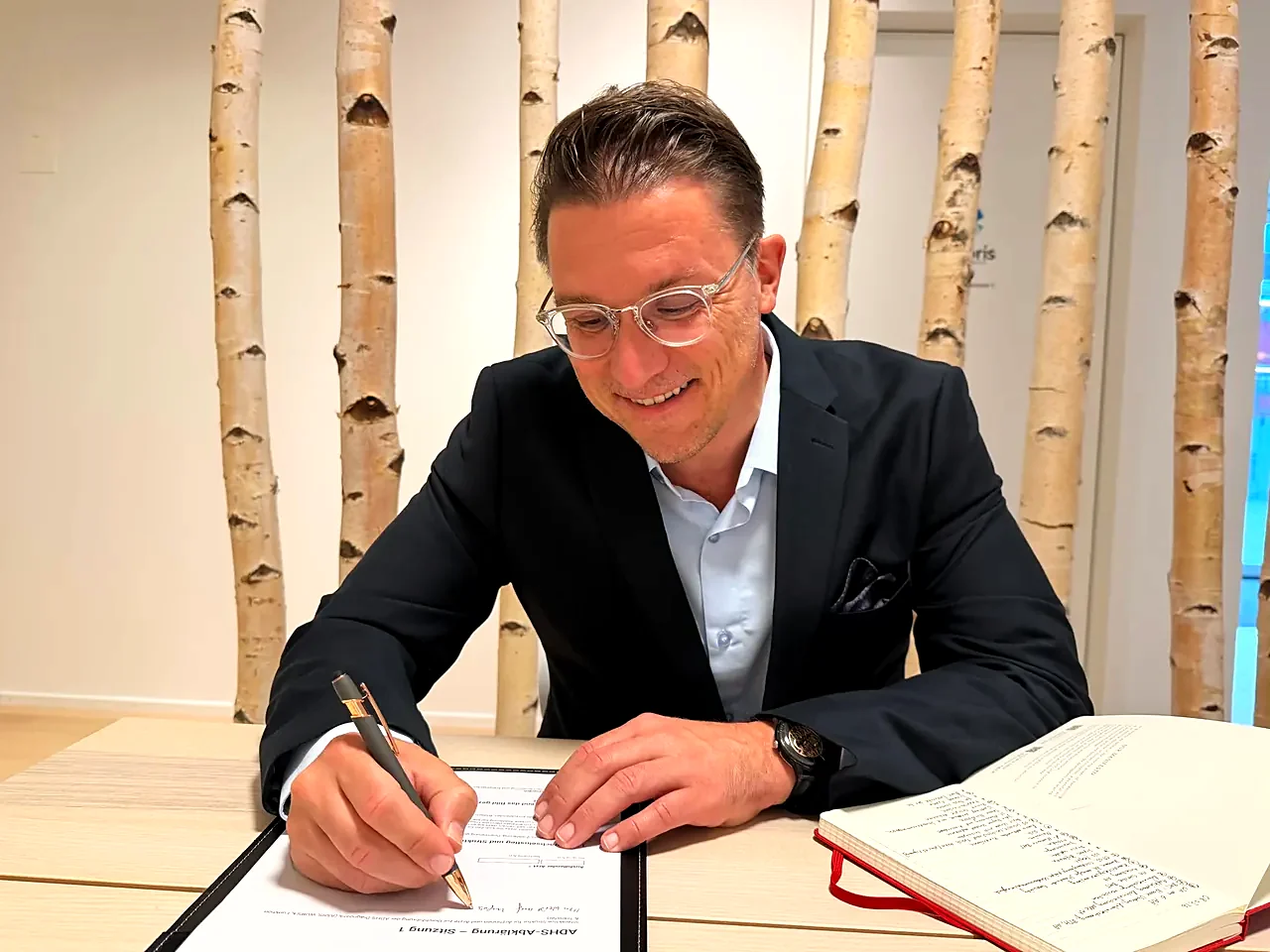 Dirk Sikorski arbeitet am Schreibtisch der klaro ADHS Praxis in Zürich, im Hintergrund Birkenstämme