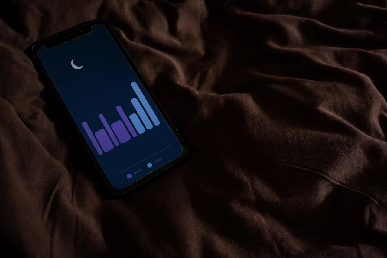 Smartphone mit Schlaftracker-Auswertung auf dunklem Bettlaken
